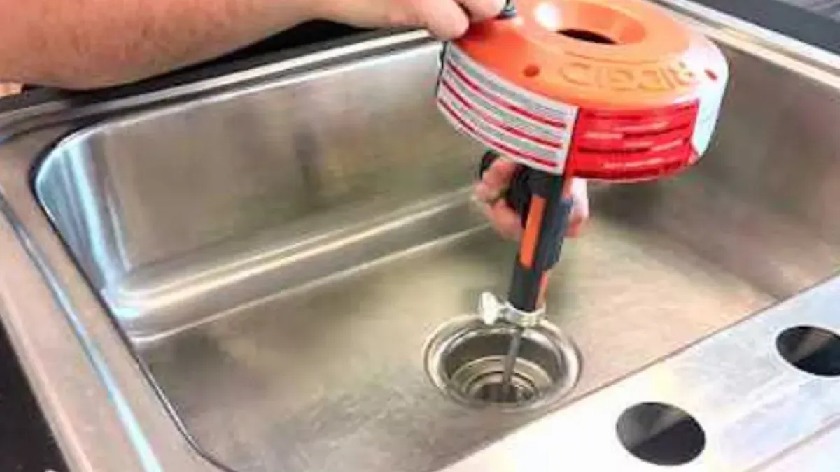 Drum auger feeding its cable into a stainless steel kitchen sink drain